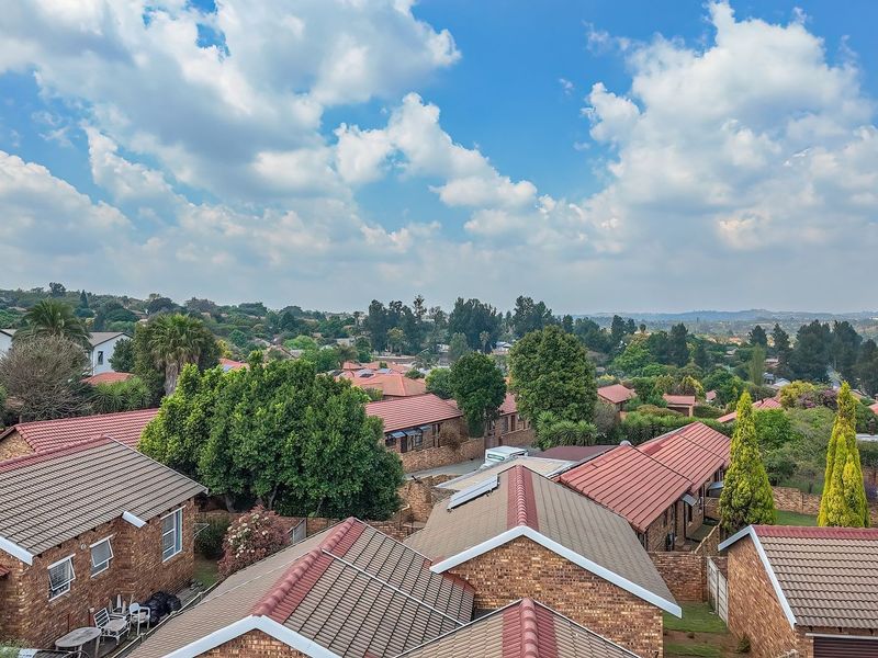 An elevated aerial view of a residential townhouse complex featuring brick buildings with tiled roofs and established surrounding greenery.