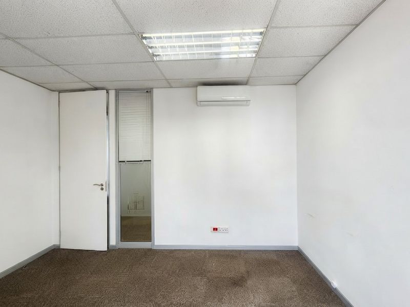 A vacant office space featuring a suspended ceiling, recessed lighting, split-system air conditioning, and carpeted flooring.
