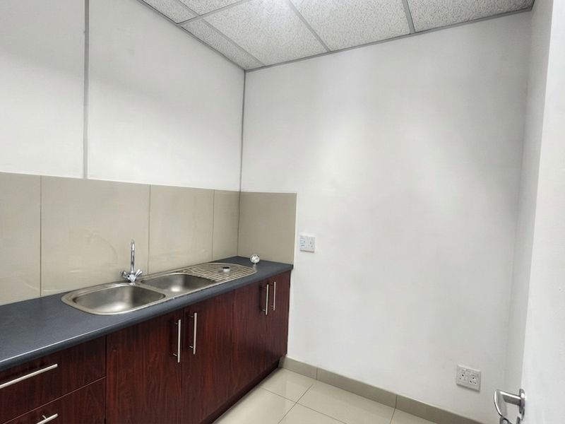 A clean and functional office kitchenette featuring dark wood cabinetry, a stainless steel sink, and neutral tiled finishes.
