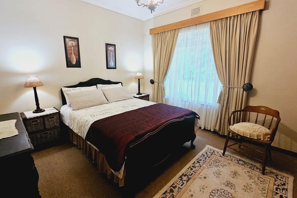 A cozy bedroom featuring neutral wall tones, carpeted flooring, and large window treatments with a wooden pelmet.