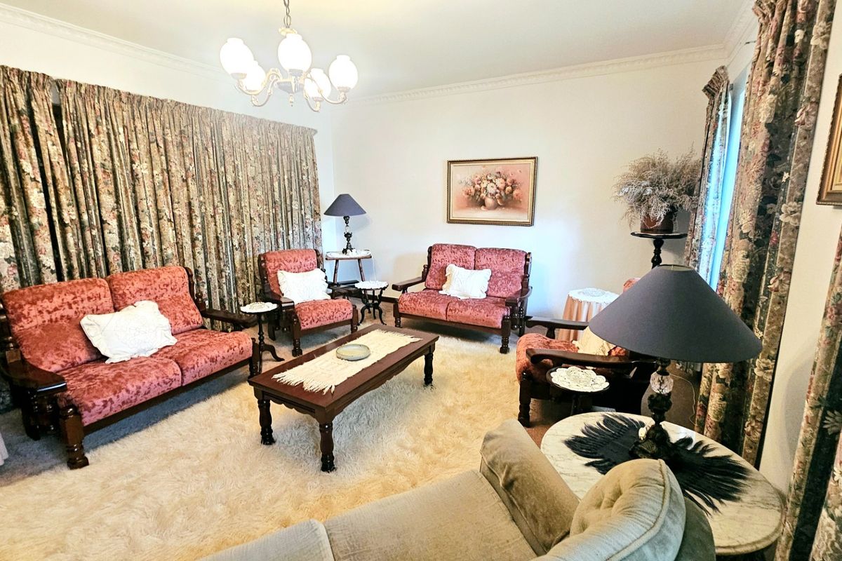A traditional living room featuring decorative ceiling cornicing and a central chandelier, offering a classic layout with ample space for seating.