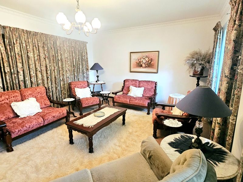 A traditional living room featuring decorative ceiling cornicing and a central chandelier, offering a classic layout with ample space for seating.