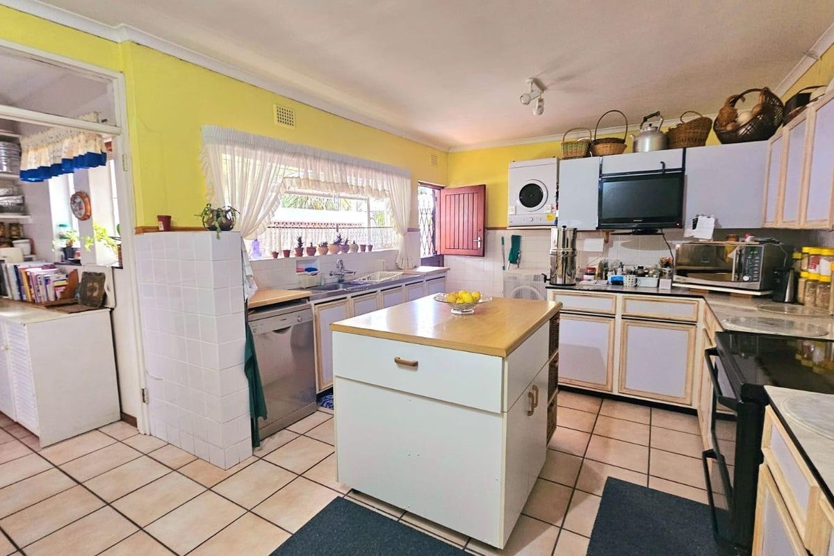 A functional kitchen featuring a central island, tiled flooring, ample cabinetry, and a separate scullery area, offering a practical layout for daily meal preparation.