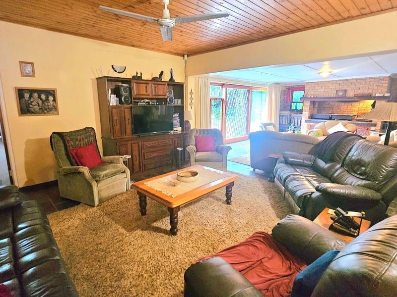 Spacious living room featuring a timber-clad ceiling, ceiling fan, and a traditional brick fireplace, with direct access to an outdoor patio area.