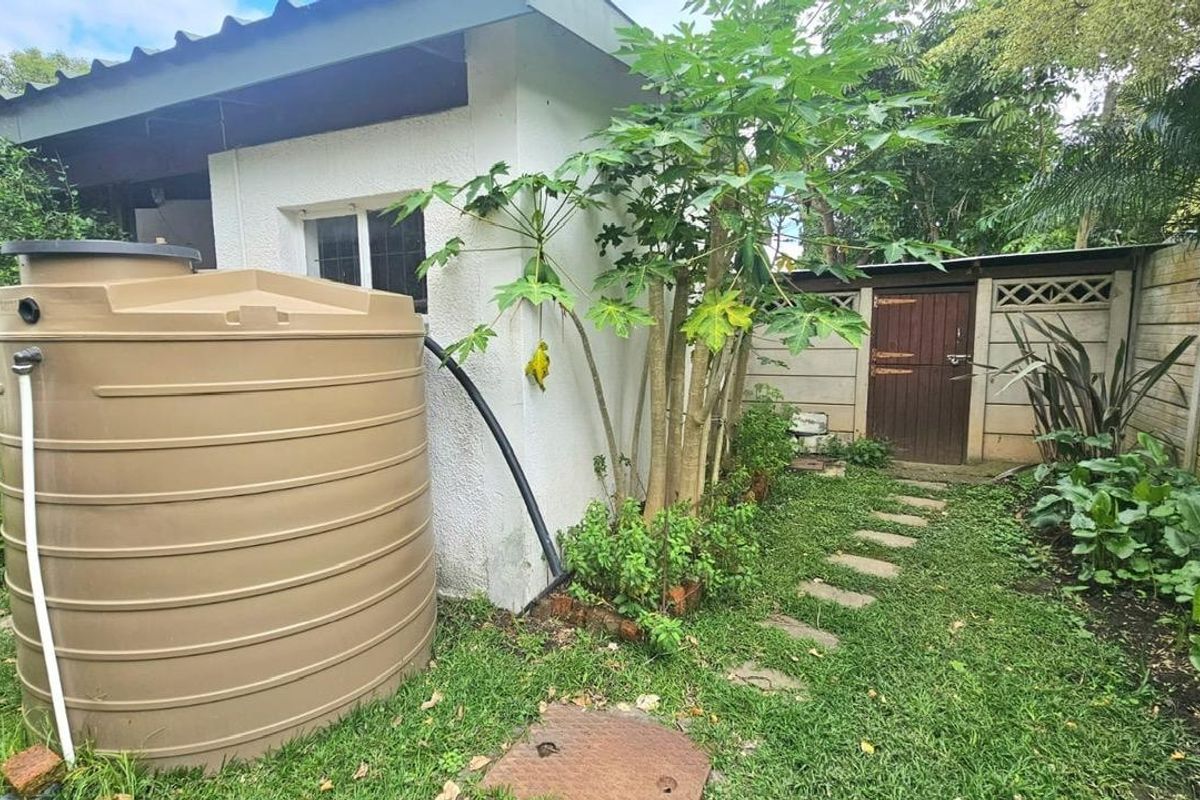 Rear exterior area featuring a large water storage tank, a paved pathway, and a timber gate set within a precast concrete boundary wall.