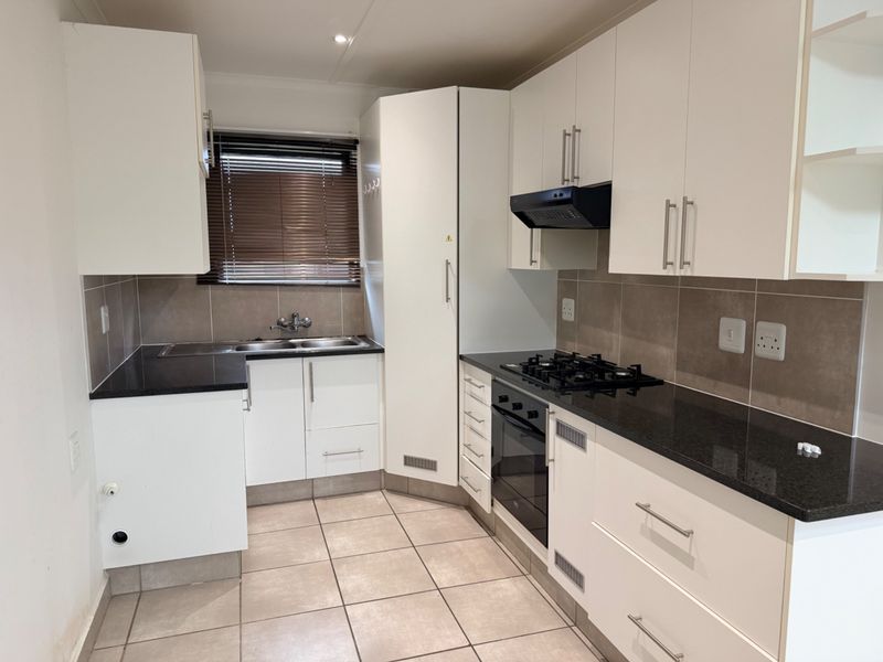 A clean, modern kitchen featuring white cabinetry, black granite countertops, a gas hob, built-in oven, and tiled flooring.