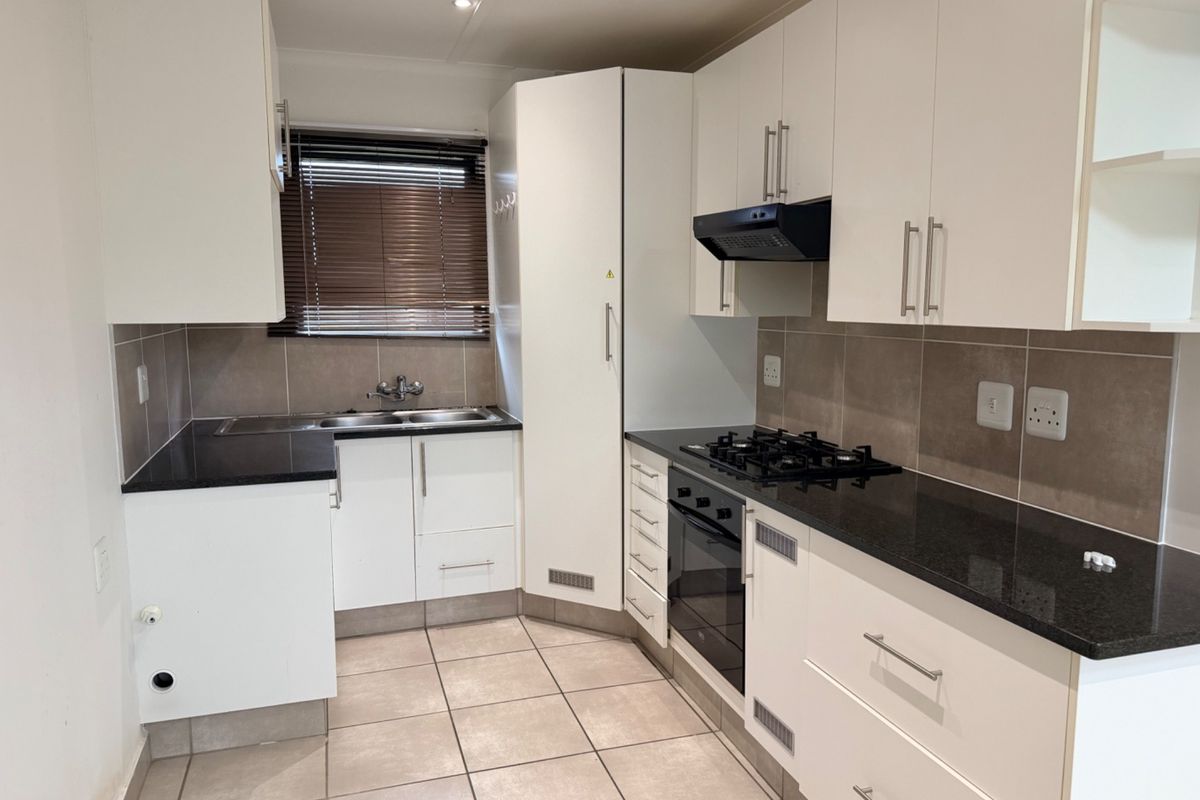 A clean, modern kitchen featuring white cabinetry, black granite countertops, a gas hob, built-in oven, and tiled flooring.