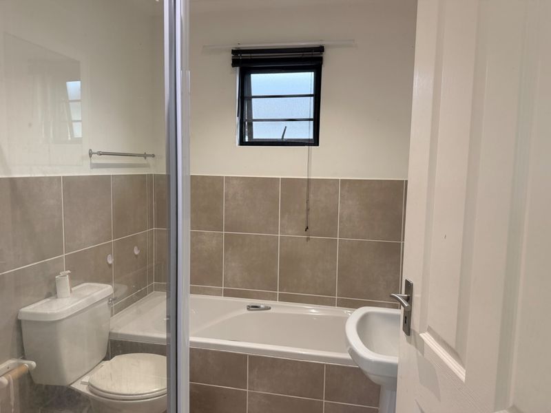 A functional bathroom featuring a bathtub, pedestal sink, and toilet with neutral wall tiling and a small window.