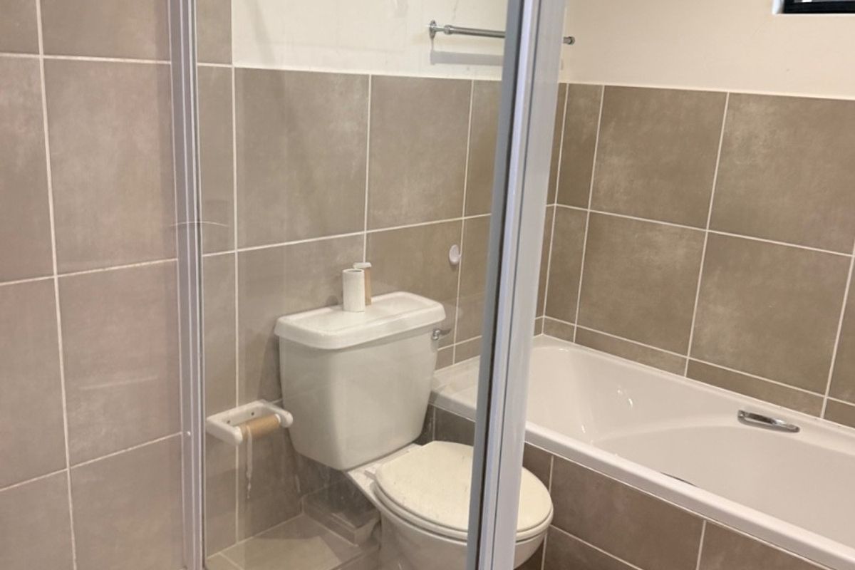 A clean, neutral-toned bathroom featuring a combined shower and bathtub, tiled finishes, and standard sanitary ware.