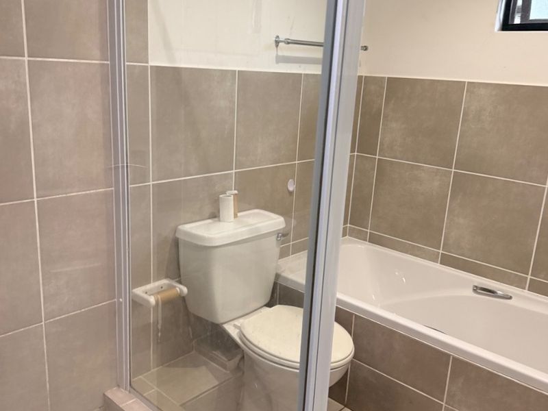 A clean, neutral-toned bathroom featuring a combined shower and bathtub, tiled finishes, and standard sanitary ware.