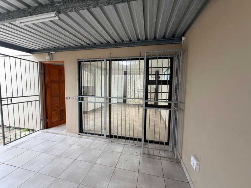 A covered patio area featuring tiled flooring, a timber entrance door, and security gates providing access to the interior living space.