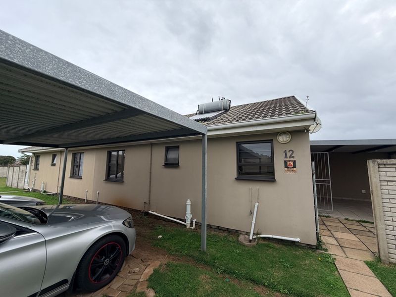 Exterior view of the property featuring a carport, solar water heating system, and paved walkway access.