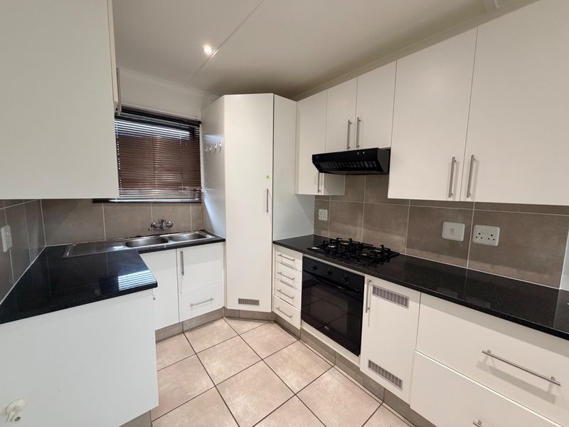 A clean, modern kitchen featuring white cabinetry, black granite countertops, a gas hob, built-in oven, and neutral tiled flooring.