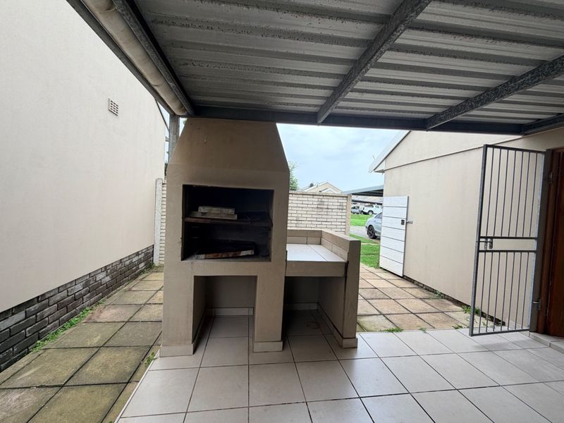 Covered outdoor patio area featuring a built-in braai, tiled flooring, and direct access to the rear yard.