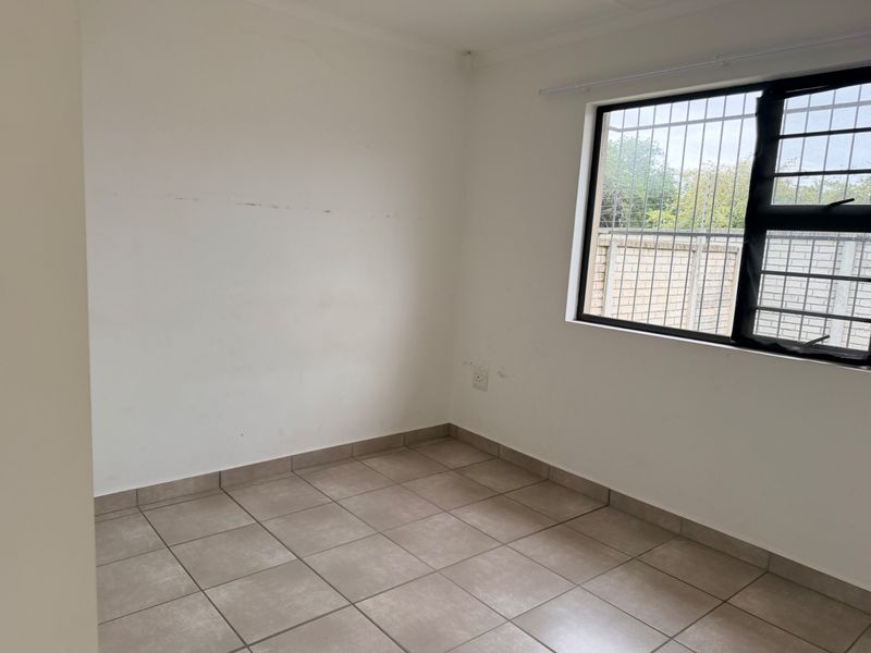 An empty bedroom featuring neutral tiled flooring and a window fitted with security bars, offering a blank canvas for personalization.