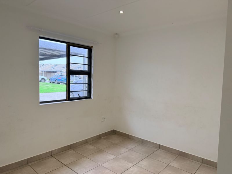 A vacant bedroom featuring neutral tiled flooring, a window with security bars, and recessed lighting, offering a clean canvas for personalization.