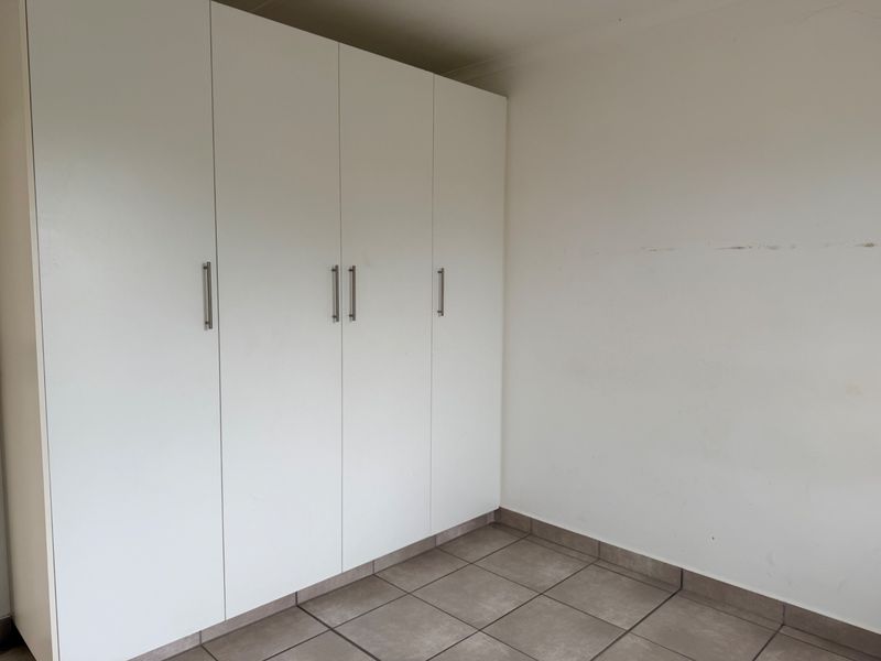 A clean, empty bedroom featuring neutral tiled flooring and ample built-in cupboard storage space.