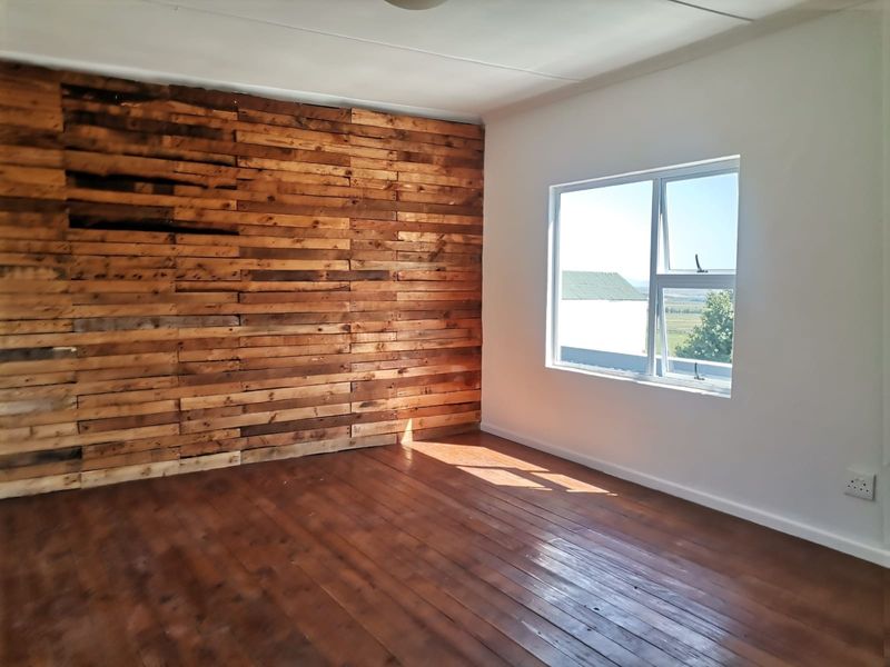 A bright, empty bedroom featuring a rustic timber accent wall, polished timber flooring, and a large window providing natural light.