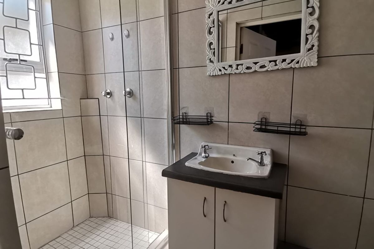A functional bathroom featuring a shower enclosure, vanity cabinet with basin, and neutral wall tiling.