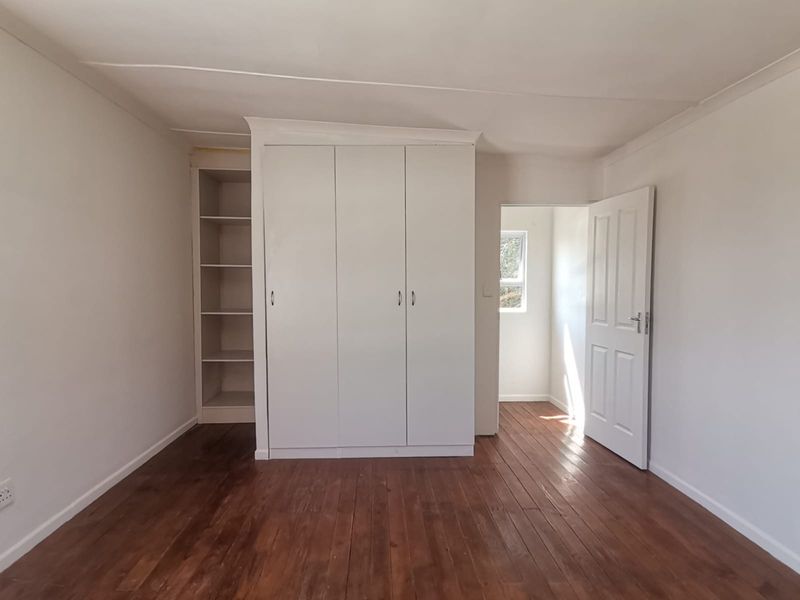 A bright, empty bedroom featuring polished timber flooring, built-in wardrobe storage, and integrated shelving units.