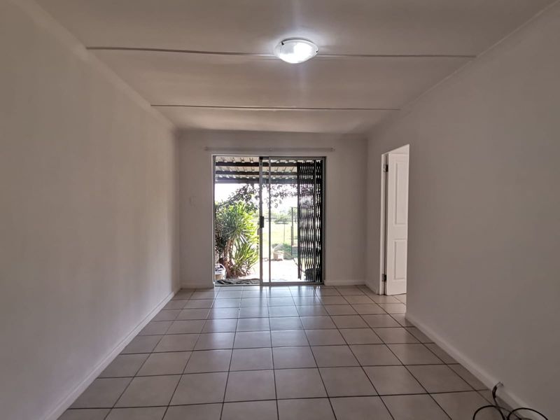 A bright, empty living room featuring neutral tiled flooring and a sliding glass door that provides direct access to the outdoor area.