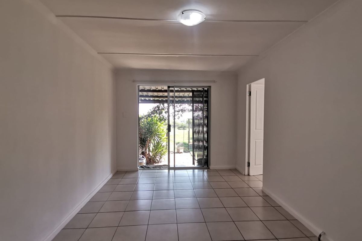 A bright, empty living room featuring neutral tiled flooring and a sliding glass door that provides direct access to the outdoor area.