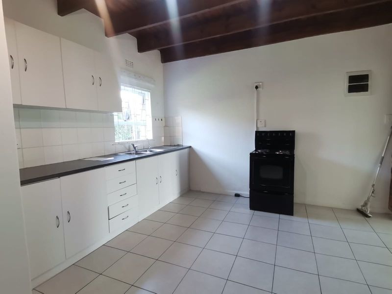 A functional kitchen featuring white cabinetry, tiled flooring, and exposed timber ceiling beams, providing a clean canvas for potential modern updates.