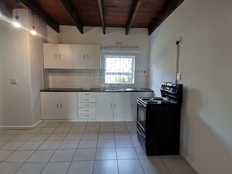A functional kitchen featuring white cabinetry, tiled backsplash, double basin sink, and exposed timber ceiling beams, providing a clean and practical workspace.