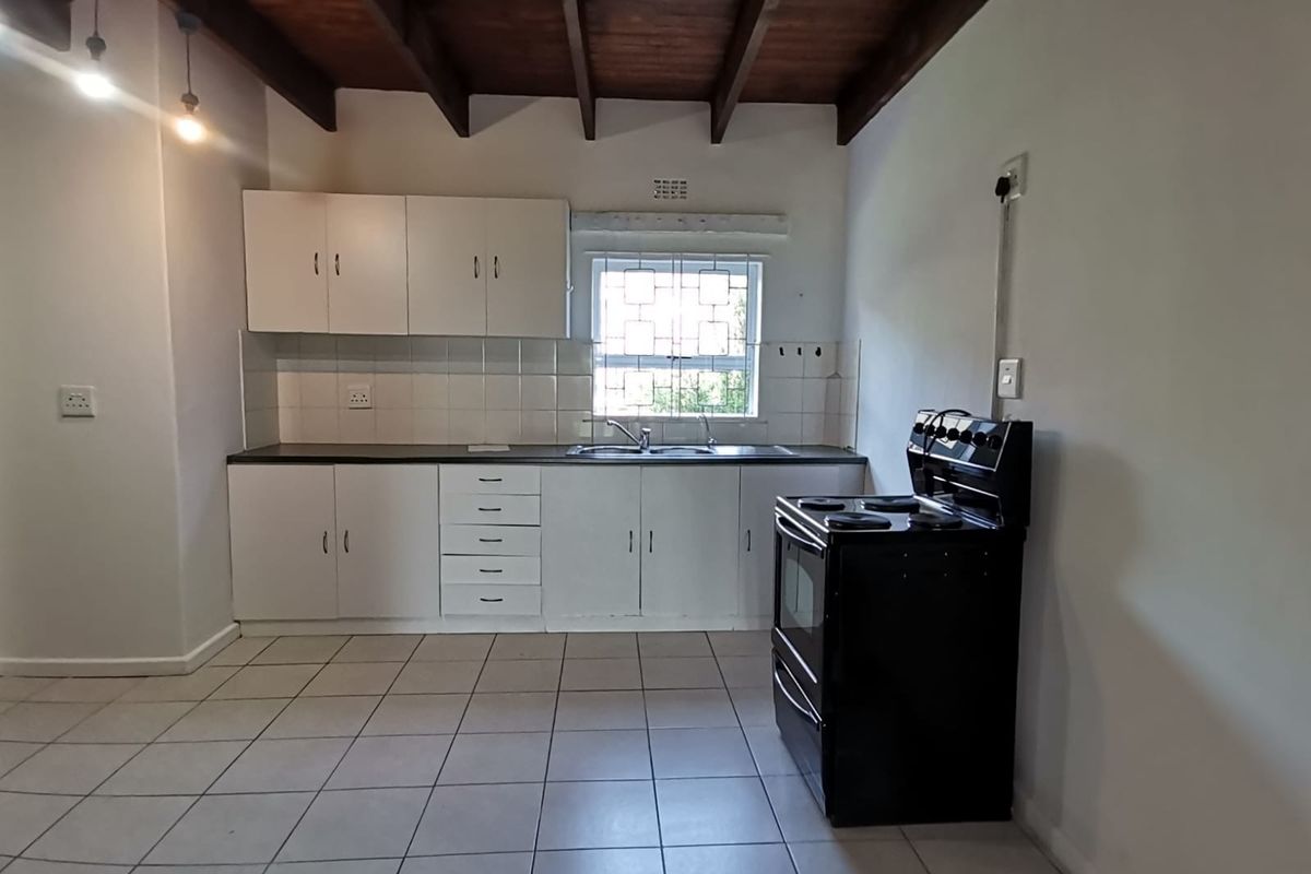 A functional kitchen featuring white cabinetry, tiled backsplash, double basin sink, and exposed timber ceiling beams, providing a clean and practical workspace.