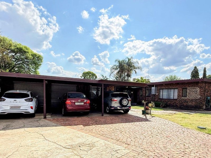 Front exterior view of a brick house featuring a multi-car carport, paved driveway, and established lawn area.