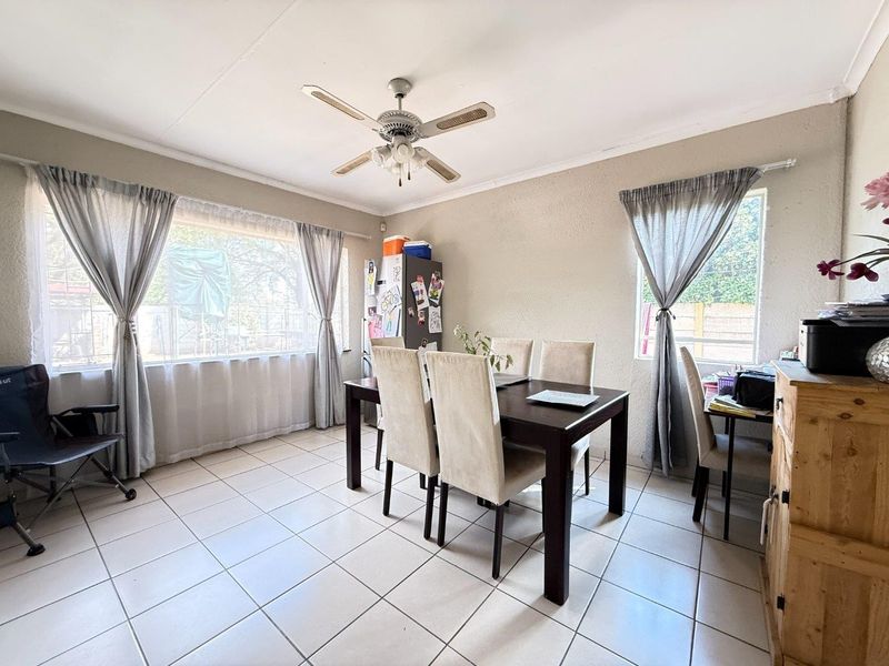A bright dining area featuring tiled flooring, a ceiling fan, and large windows that provide ample natural light.