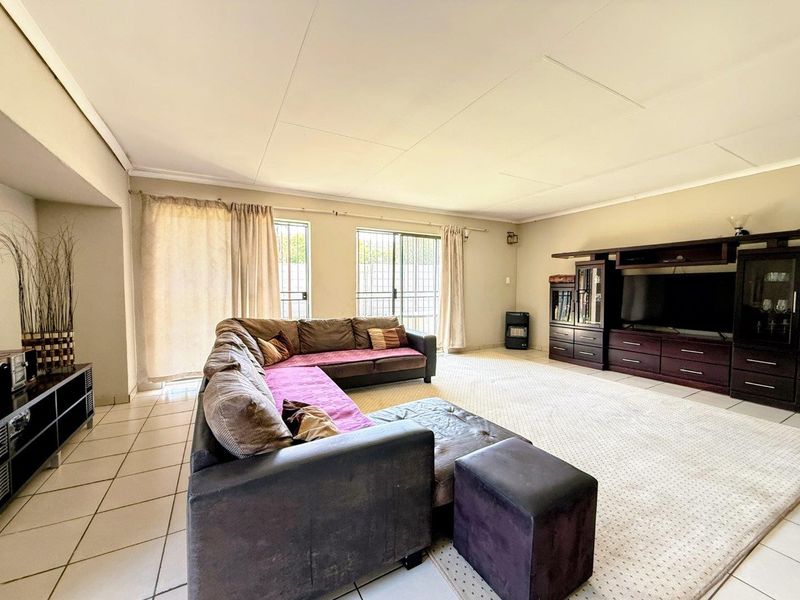 Spacious living room featuring tiled flooring, large sliding glass doors with security gates, and integrated built-in cabinetry for storage and media display.