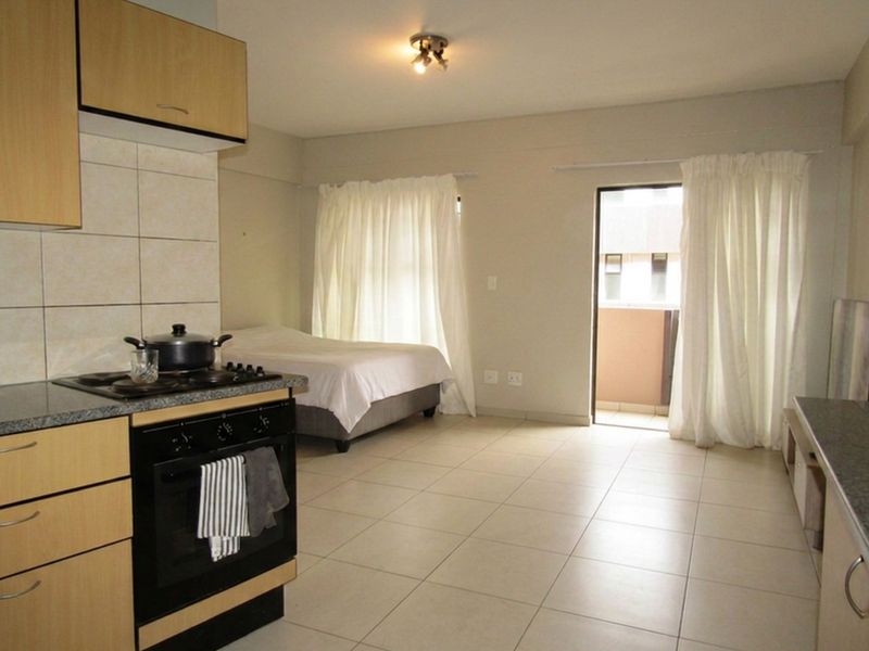 Open-plan studio apartment featuring a functional kitchen with built-in cabinetry, tiled flooring throughout, and direct access to a private balcony.