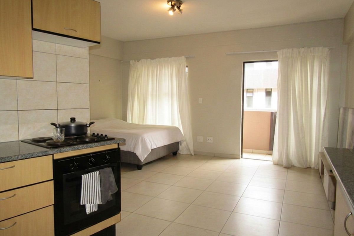 Open-plan studio apartment featuring a functional kitchen with built-in cabinetry, tiled flooring throughout, and direct access to a private balcony.