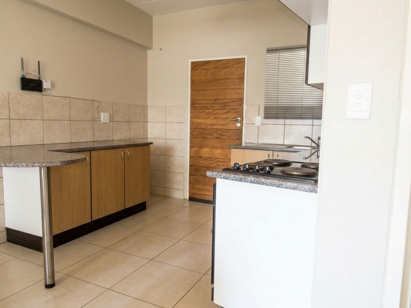 A functional kitchen featuring built-in cabinetry, granite countertops, a hob, and tiled finishes, offering a clean and practical workspace.