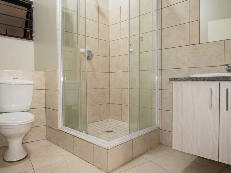 A functional bathroom featuring a corner shower enclosure, a vanity cabinet with a granite countertop, and neutral wall and floor tiling.