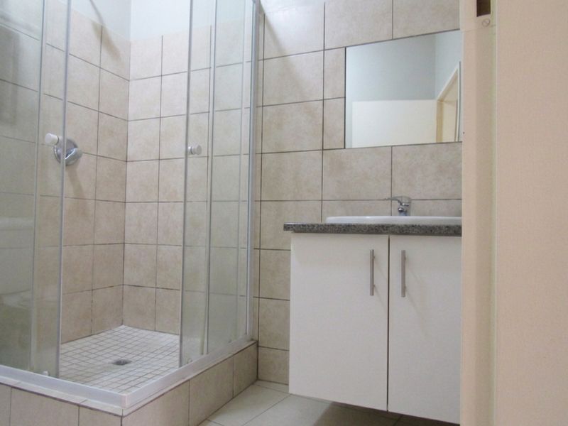 A clean, functional bathroom featuring a glass-enclosed shower, a modern vanity cabinet with a basin, and neutral wall tiling.