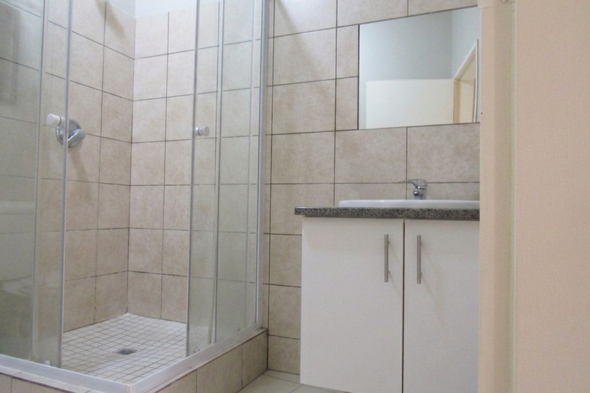 A clean, functional bathroom featuring a glass-enclosed shower, a modern vanity cabinet with a basin, and neutral wall tiling.