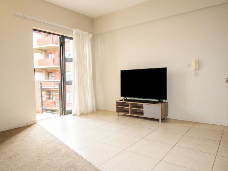 A bright living room featuring neutral tiled flooring and direct access to a private balcony through a sliding glass door.