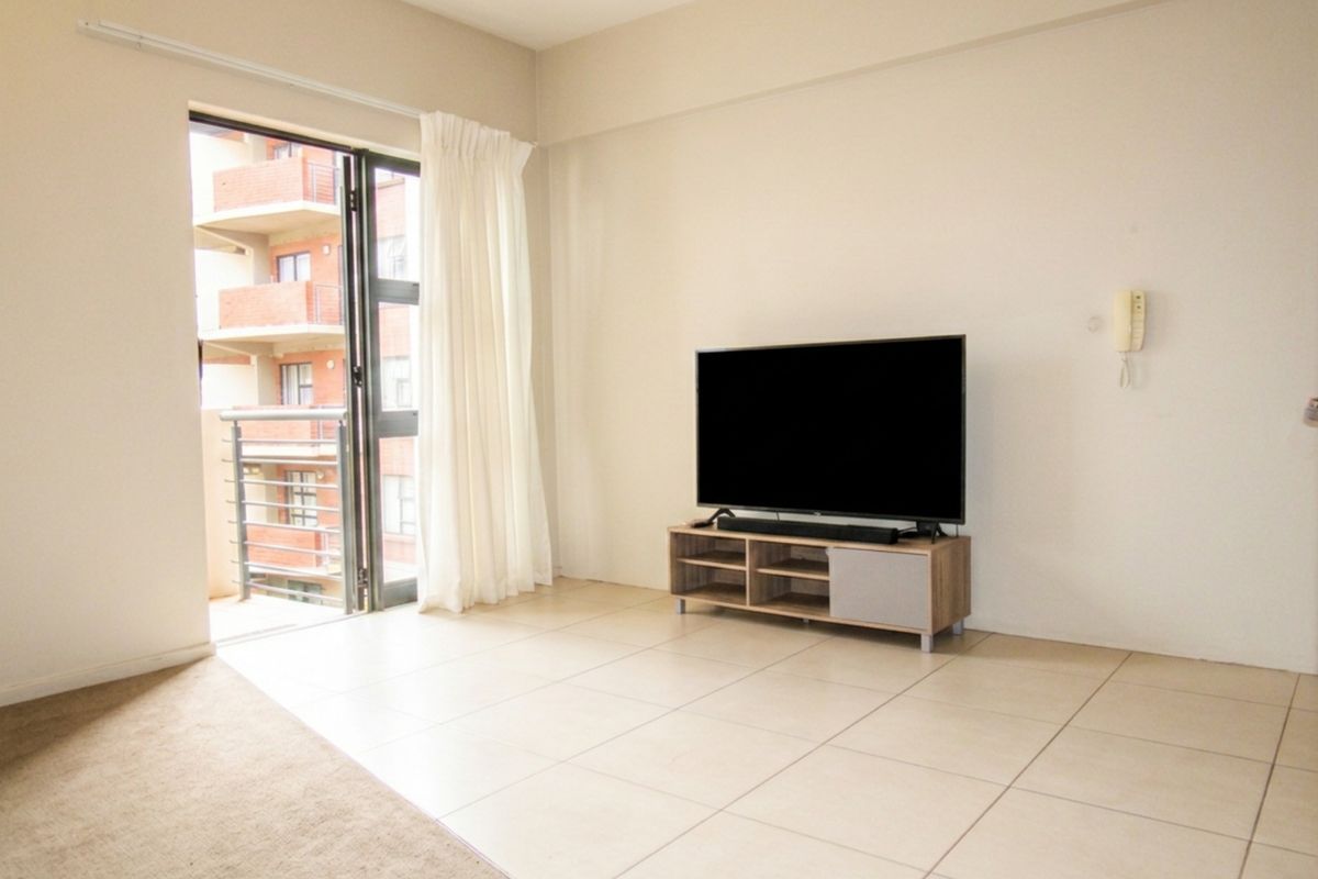 A bright living room featuring neutral tiled flooring and direct access to a private balcony through a sliding glass door.