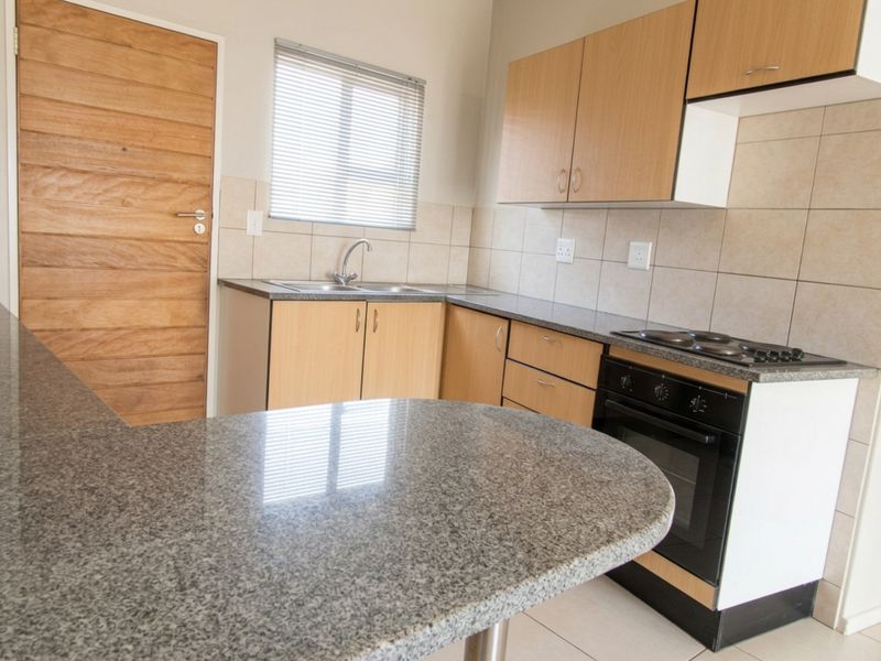 A functional kitchen featuring laminate cabinetry, granite countertops, a built-in oven with electric hob, and a tiled backsplash.