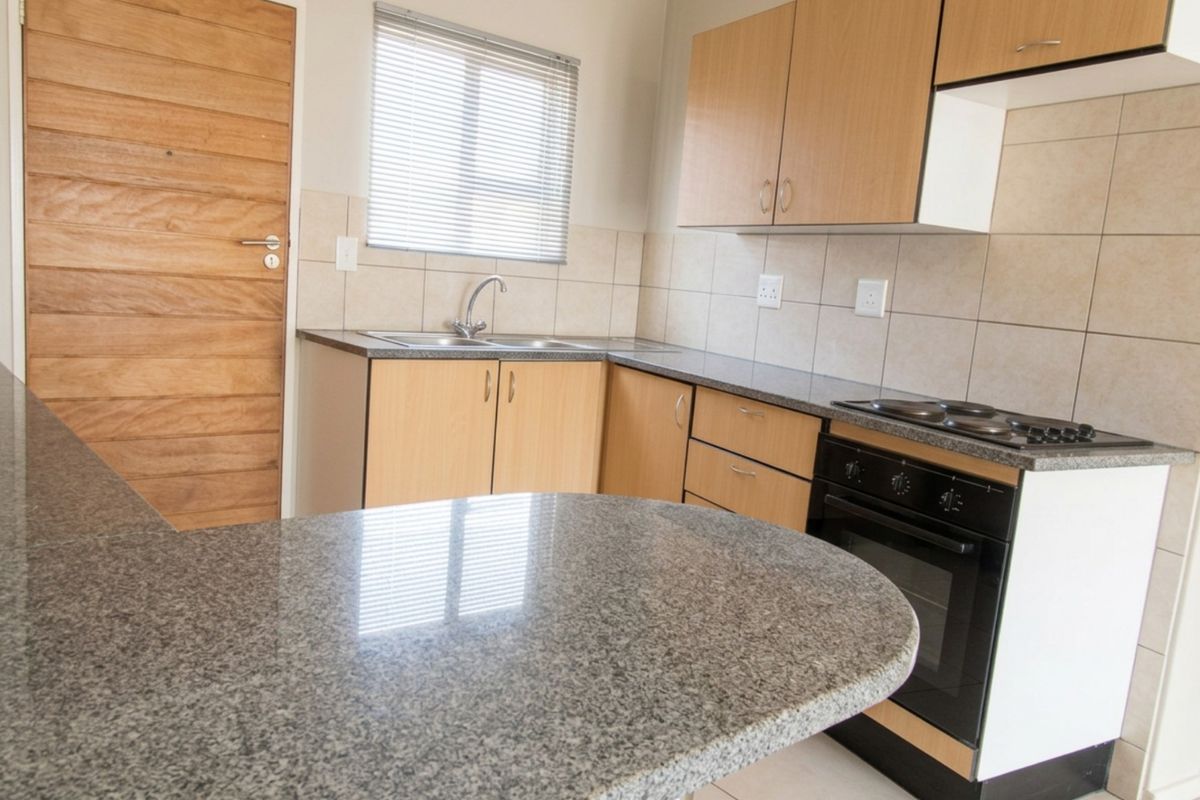 A functional kitchen featuring laminate cabinetry, granite countertops, a built-in oven with electric hob, and a tiled backsplash.