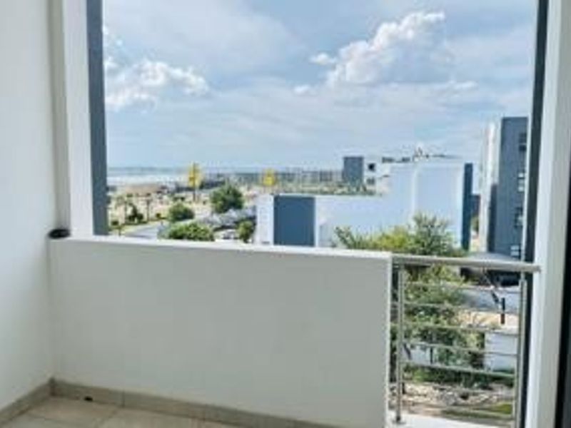A clean, modern balcony featuring tiled flooring and a stainless steel balustrade, offering an open view of the surrounding neighborhood and landscape.