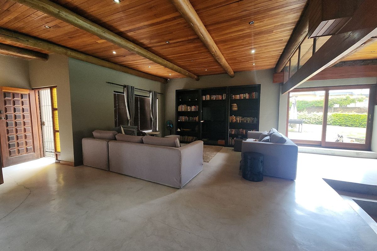 Spacious living room featuring a high exposed timber beam ceiling, polished concrete floors, and large sliding glass doors providing access to the garden.