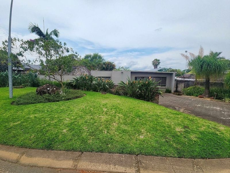 Front view of the property featuring a well-maintained lawn, landscaped garden beds, and a paved driveway leading to the residence.