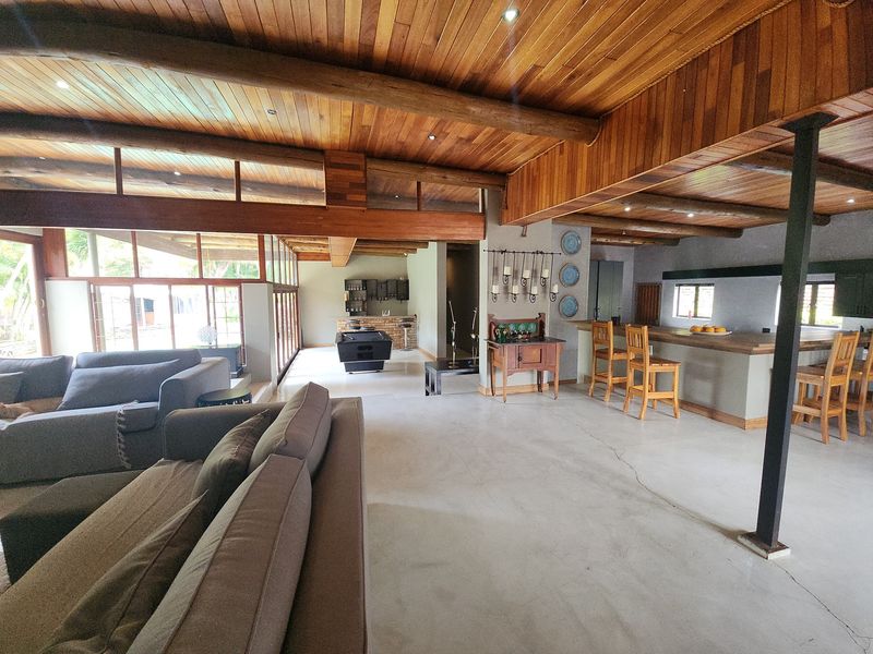 Spacious open-plan living area featuring a striking exposed timber beam ceiling, polished concrete floors, and a built-in breakfast bar with integrated lighting.