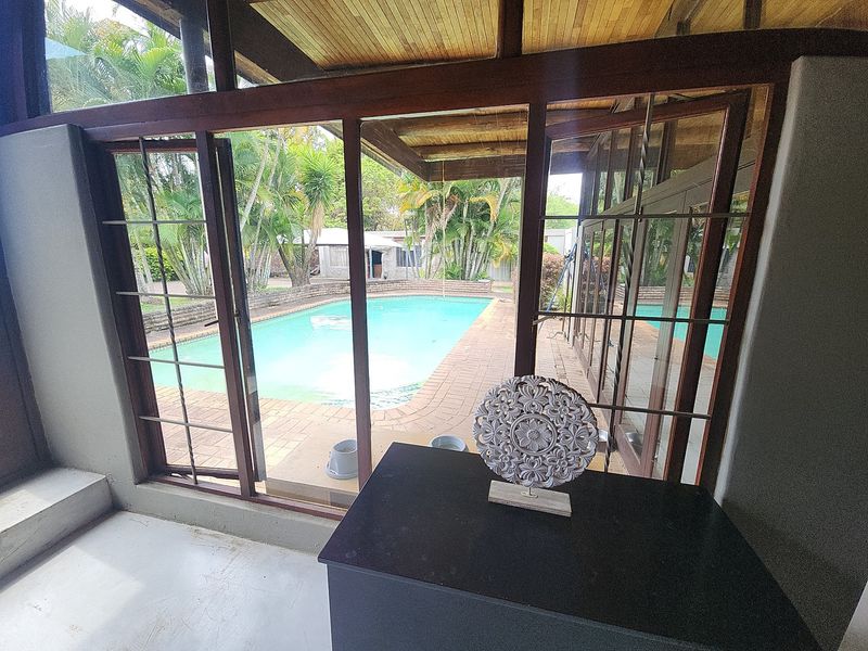 Covered patio area featuring timber-framed glass doors opening directly onto a brick-paved pool deck and swimming pool.