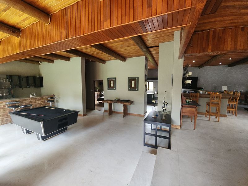 Spacious open-plan living area featuring exposed timber beam ceilings, polished concrete floors, and a built-in brick bar, creating a rustic and inviting atmosphere.