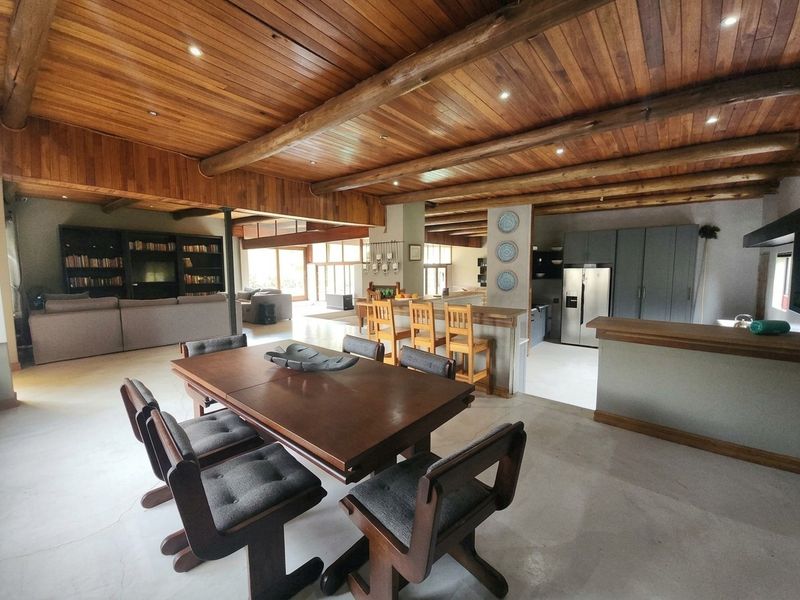 Spacious open-plan living and dining area featuring a striking timber-clad vaulted ceiling with exposed beams, polished concrete floors, and a modern integrated kitchen.
