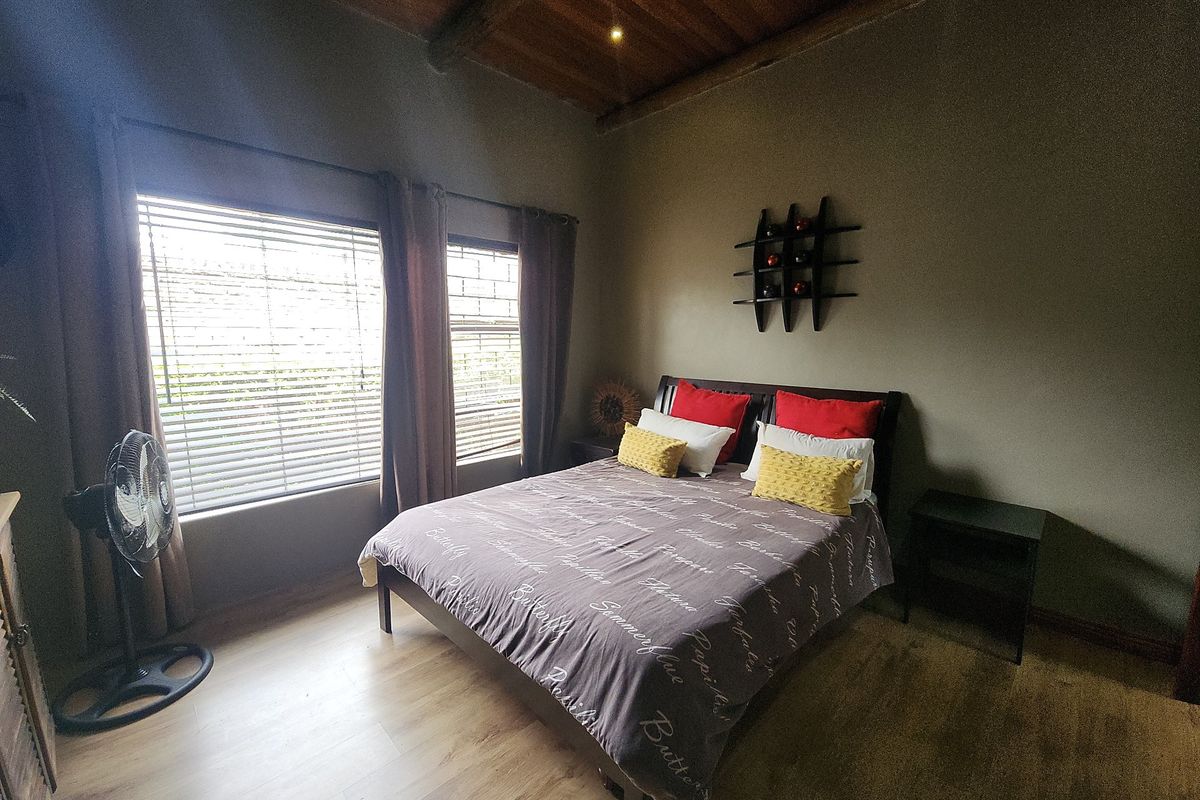 A comfortable bedroom featuring exposed timber ceiling beams, laminate flooring, and large windows fitted with venetian blinds and security bars.